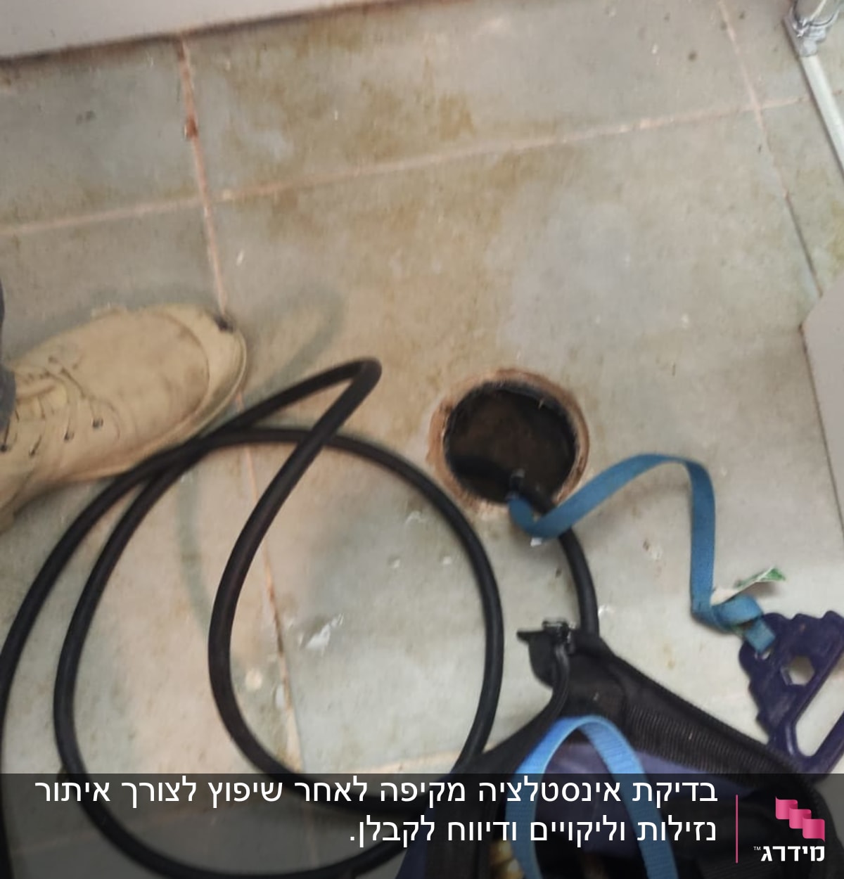 צינור שחור וכלי עבודה ליד פתח ניקוז ברצפה